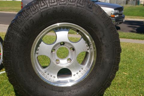 1986 Ford Bronco - A close-up of a tire and wheel assembly is shown with a silver SUV in the background.