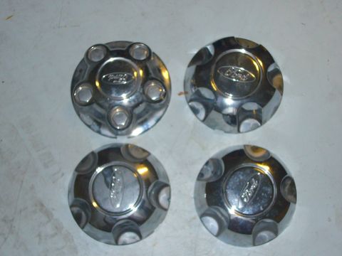 2000 Ford Crown Victoria - Four chrome Ford hubcaps are displayed on a flat surface.