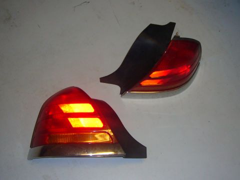 2000 Ford Crown Victoria - Two red tail lights, likely for a sedan, are shown with chrome trim and black plastic components.