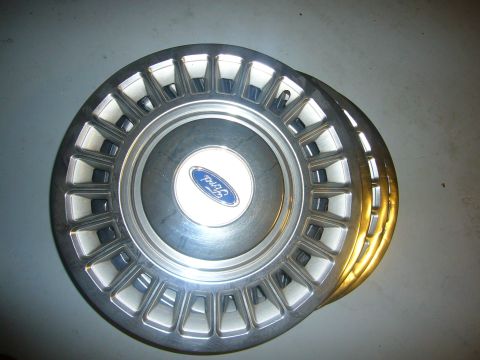 2000 Ford Crown Victoria - A set of four Ford hubcaps are shown stacked on a gray surface.