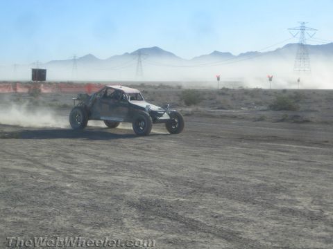 1990 Ford Bronco - off-road race buggy throws up dust as it speeds across a flat desert course beneath power lines and mountains.