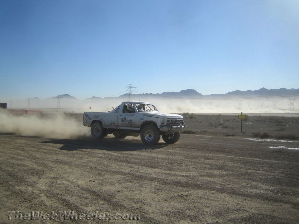 White pickup truck racing through desert flats kicking up dust near power lines