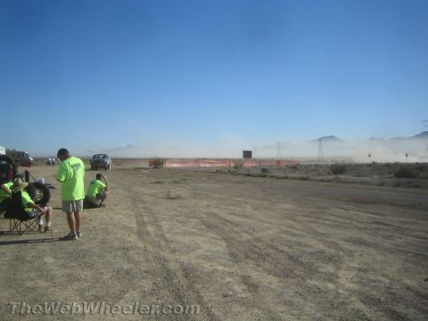 1990 Ford Bronco - Onlookers in green shirts watch distant dust plumes over an orange-fenced desert race course on a clear day.