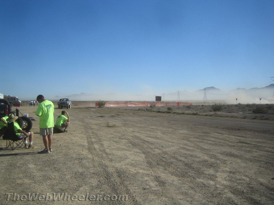 People watching dust rise across a desert off-road course under blue sky