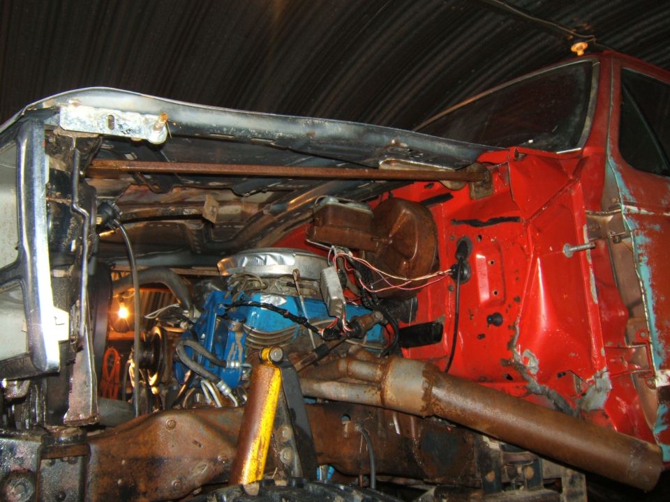 Truck engine bay with blue engine block, rusty exhaust, and red body panels