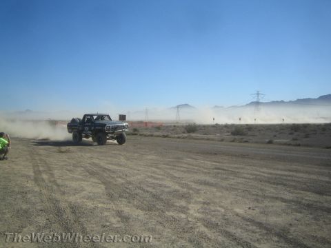 1990 Ford Bronco - numbered off-road race truck speeds across the desert kicking up a long dust trail near power-line towers.