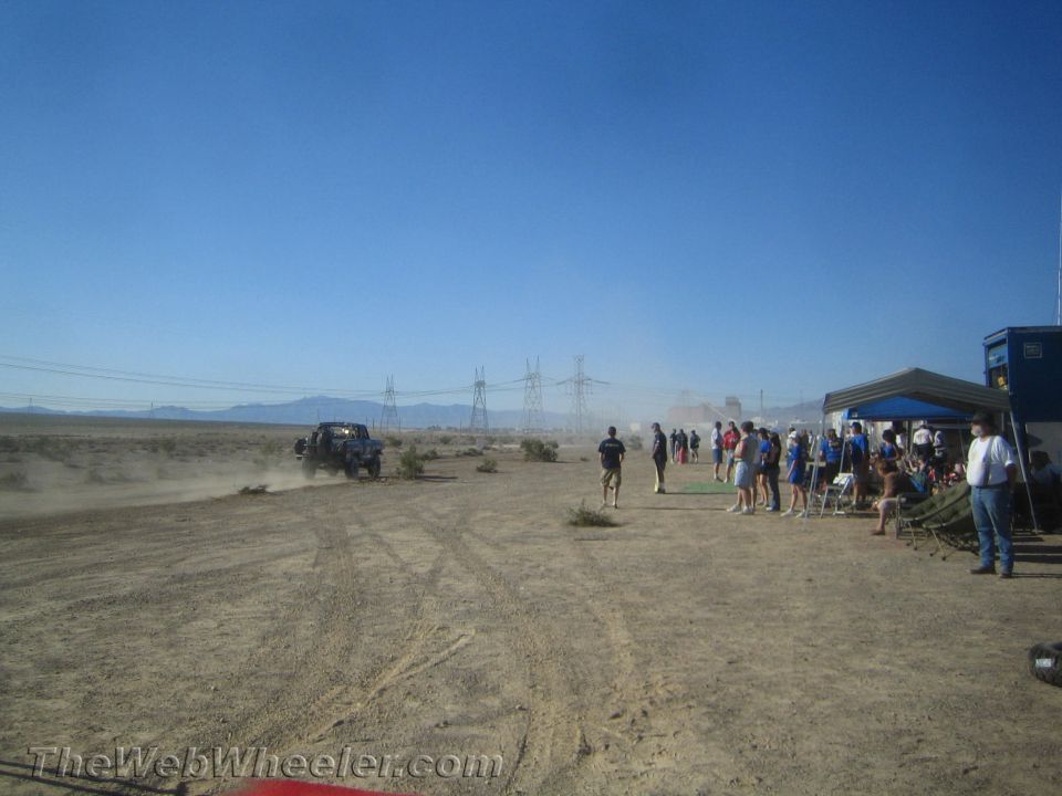 Distant off-road vehicle and crowd under canopies at a desert event