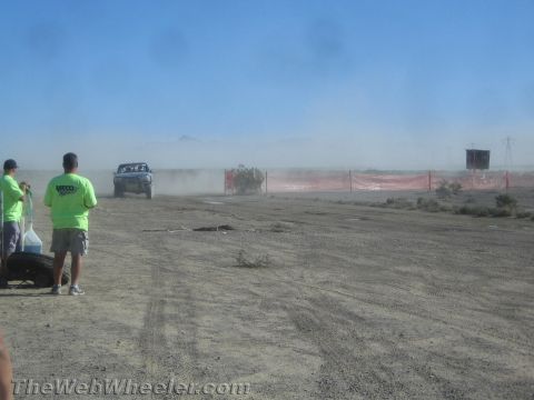 1990 Ford Bronco - off-road truck moves through a dusty haze along a desert course while spectators in green shirts look on.