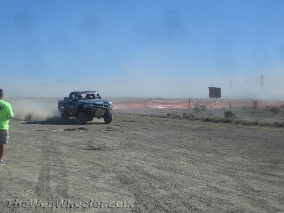 Blue off-road race truck cornering in the desert beside an orange course barrier