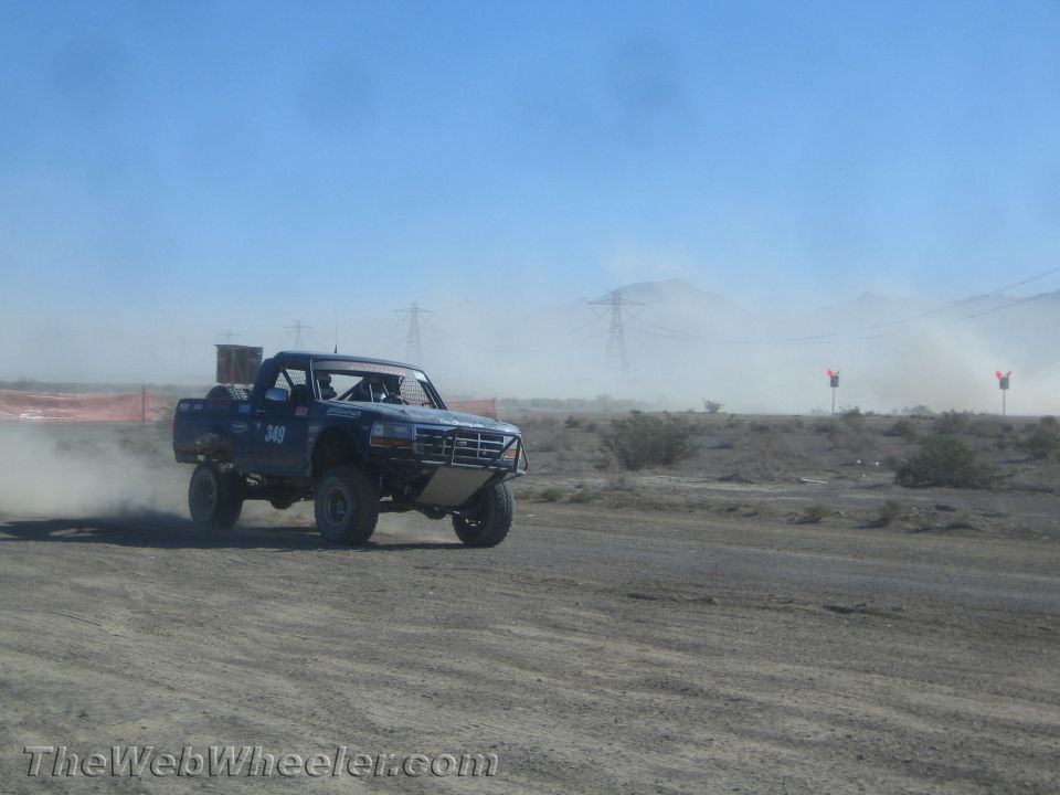 Blue number 349 prerunner truck racing across the desert with mountains behind