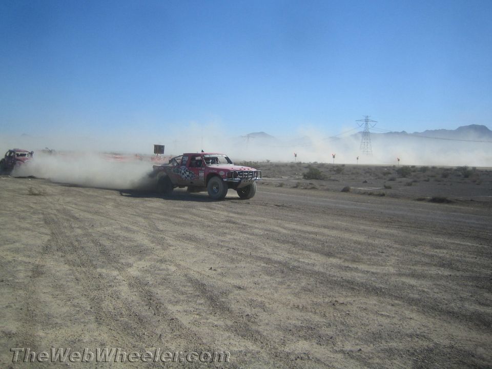 Red and white off-road race truck throwing up dust on a desert course