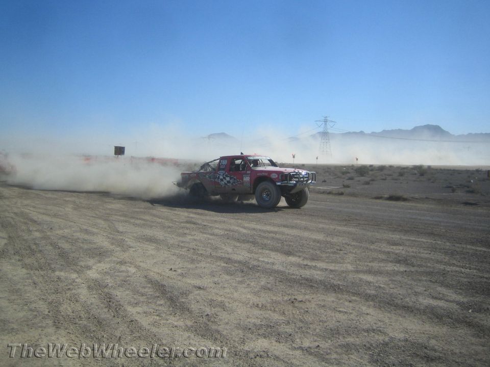 Red and white off-road race truck cornering hard in desert dust