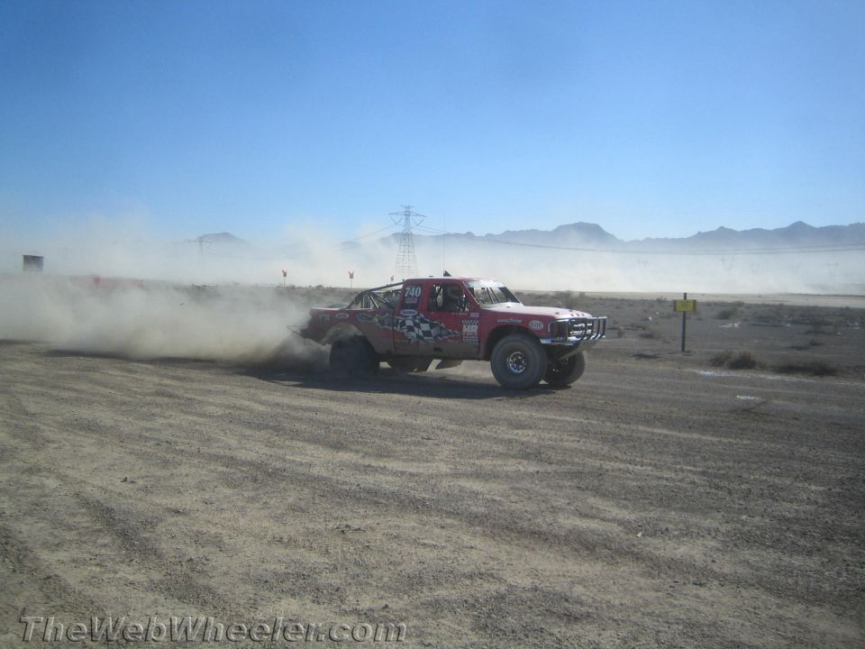 Red and white checkered off-road race truck sliding through desert dust