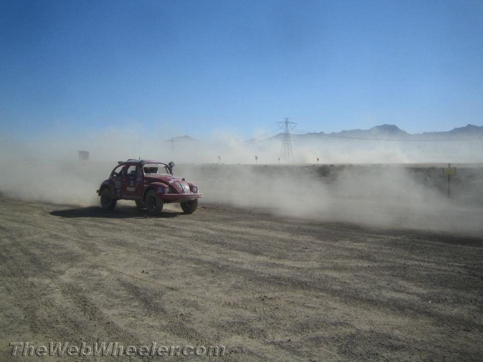 Dark red off-road Baja Bug racing through dust on a desert course