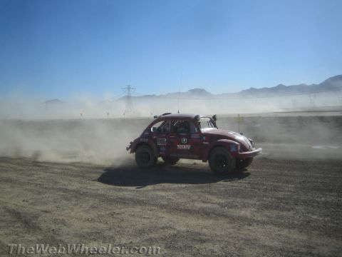 1990 Ford Bronco - Dark red Baja Bug number 1100 with a Tecate decal races across a hardpack desert track trailing dust.