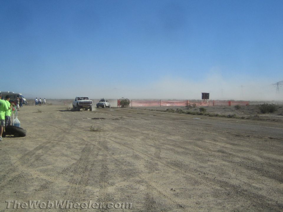 White off-road trucks racing past spectators on a desert course