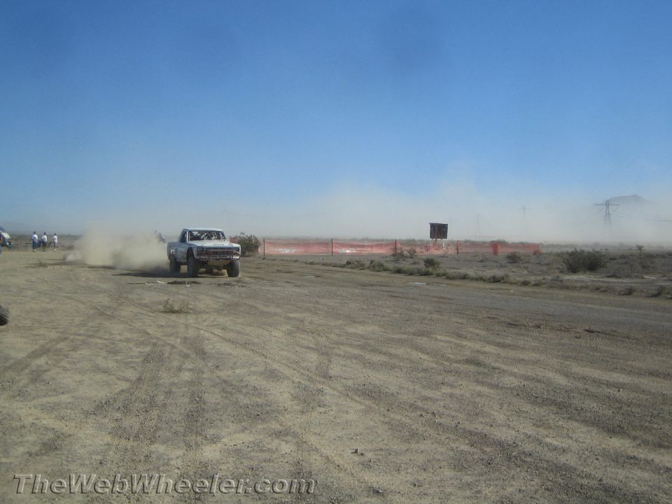 White off-road truck speeding past orange barrier fencing in the desert