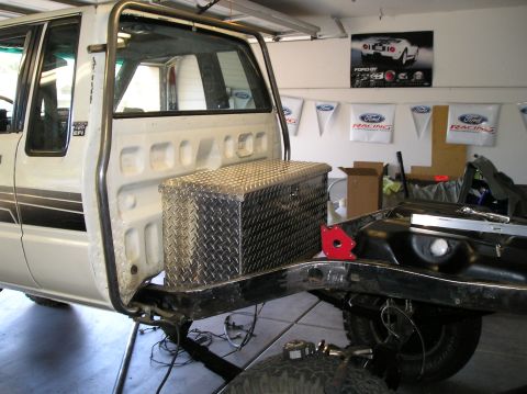 1986 Toyota Hilux - A diamond plate toolbox is secured to the frame of a pickup truck, with roll cage bars installed.