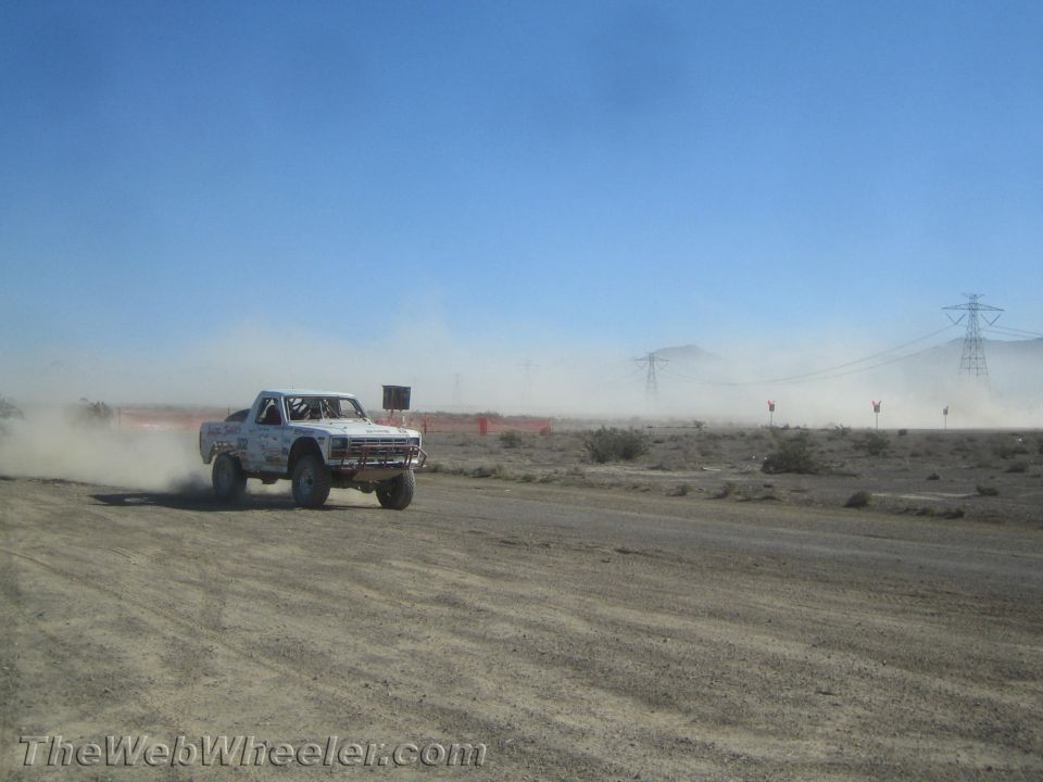 White off-road truck racing in the desert with mountains and power lines behind