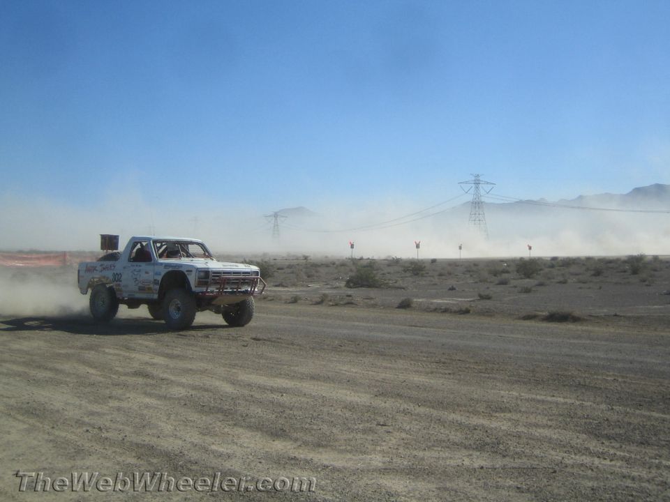 White number 302 off-road truck racing across a desert track