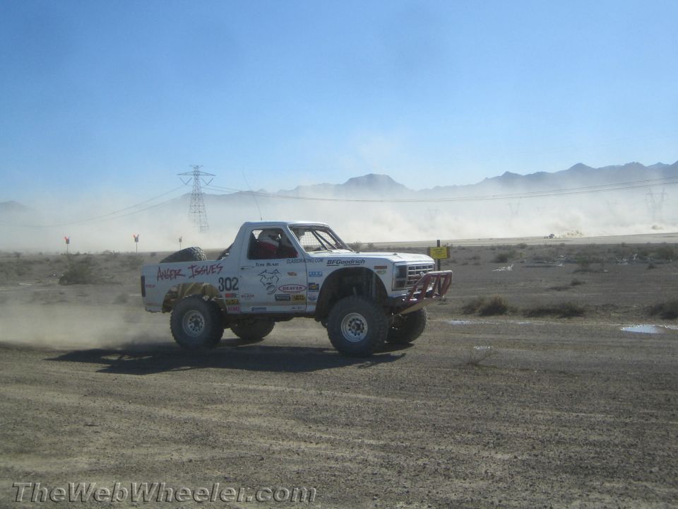 White number 302 off-road truck with sponsor decals racing in the desert