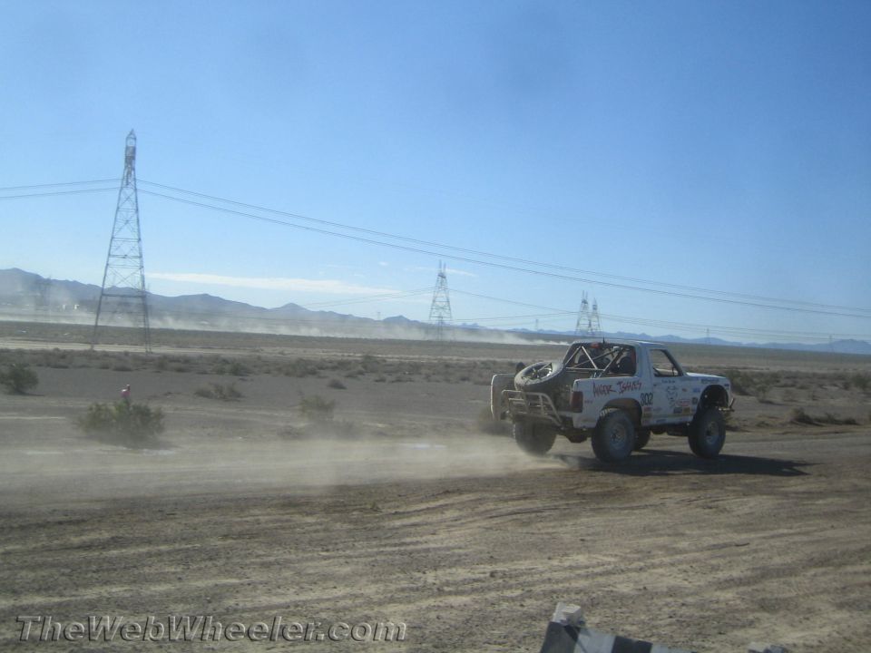 White off-road race truck speeding away on a desert course near transmission towers