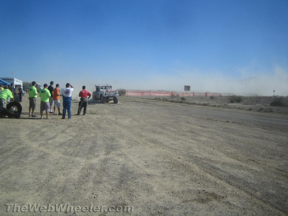 Spectators watch a light-colored off-road truck approach on a desert dirt course
