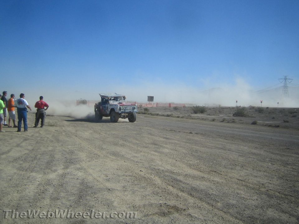White off-road race vehicle on a desert course with spectators on the left