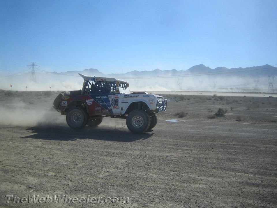 White off-road race truck number 305 racing across a dusty desert course