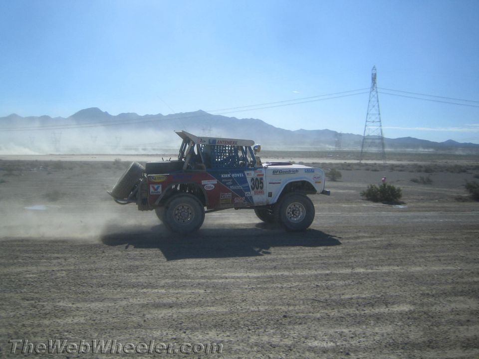 White off-road race truck 305 in motion across open desert with mountains behind