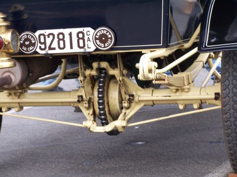 1990 Ford Bronco - Close-up of the rear axle and chain drive system on a vintage automobile, its license plate and club emblems.