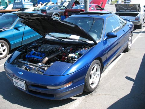 1995 Ford Probe - A blue 1995 Ford Probe is displayed with its hood open, revealing the engine. Other vehicles are visible in the background.
