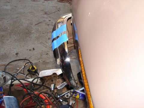 1973 Ford Ranchero - A chrome bumper end held in place with strips of blue painter's tape against a primer-tan body panel and an amber side-marker reflector, du…