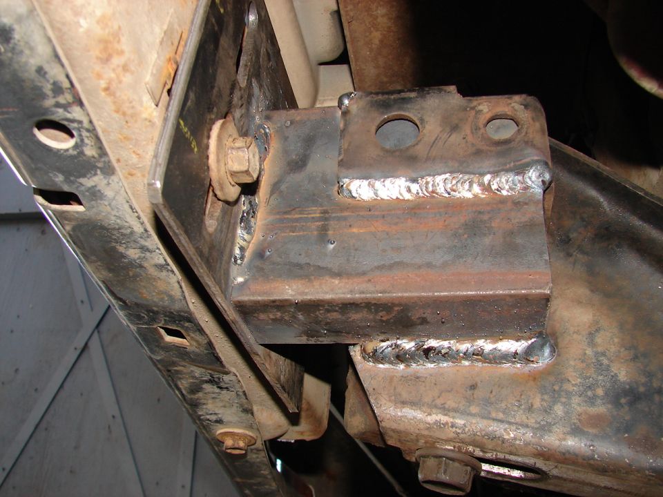 Fresh MIG welds joining a fabricated steel bracket to a rusty vehicle frame