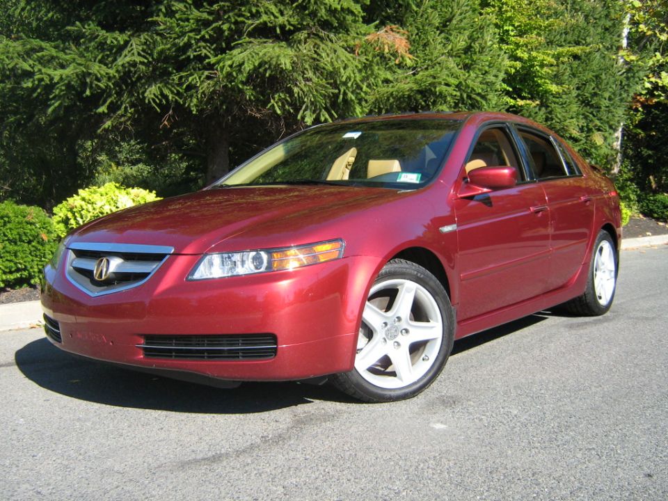 Red Acura TL sedan parked outdoors with trees in background. Front 3/4 view