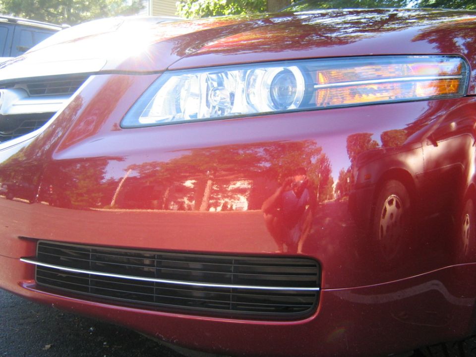 Red car front grille and headlight with reflection of another vehicle