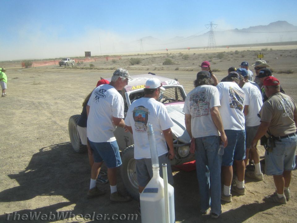 Crew in matching white shirts working around a race car in the desert pits