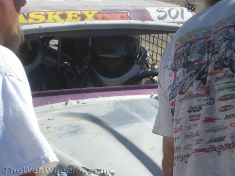 1990 Ford Bronco - driver wearing a Shoei helmet sits in the caged cockpit of a race car marked 501 as a crew member stands nearby.