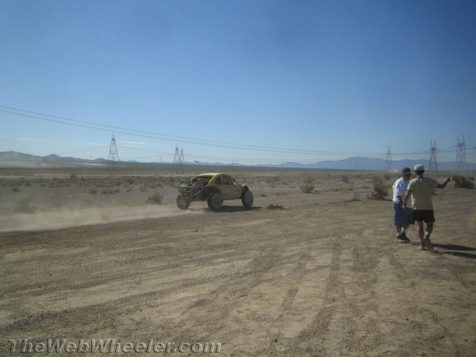 Yellow off-road buggy racing in the distance as two spectators watch