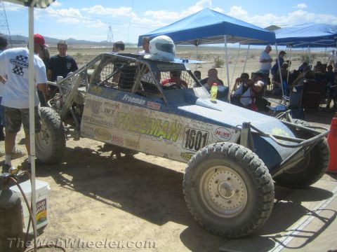 1990 Ford Bronco - silver tube-frame off-road race car lettered Freeman and numbered 1601 sits under a canopy in a desert pit area.
