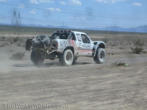 1990 Ford Bronco - white off-road race truck lettered COLLINS races across flat open desert trailing dust.