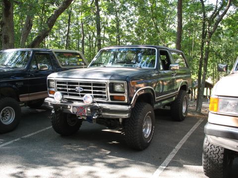 1995 Ford C-350 (Centurion Conversions) - This lifted SUV features a prominent chrome grille and off-road tires, parked in a lot with other vehicles.