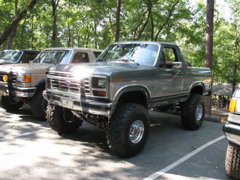 1995 Ford C-350 (Centurion Conversions) - A lifted Ford Bronco is parked in a lot with trees in the background.