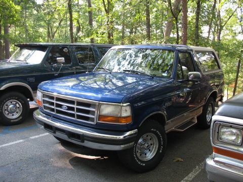 1995 Ford C-350 (Centurion Conversions) - Blue 1995 Ford Bronco parked next to other vehicles in a wooded area.