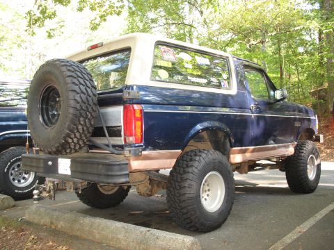1995 Ford C-350 (Centurion Conversions) - A lifted blue Ford Bronco with a spare tire mounted on the rear bumper is parked outdoors.