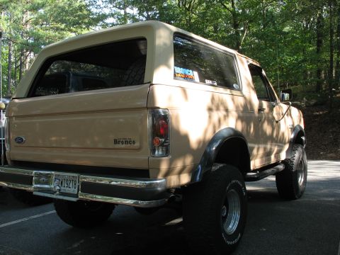 1995 Ford C-350 (Centurion Conversions) - Rear quarter view of a lifted tan Ford Bronco with off-road tires and a spare tire visible inside.
