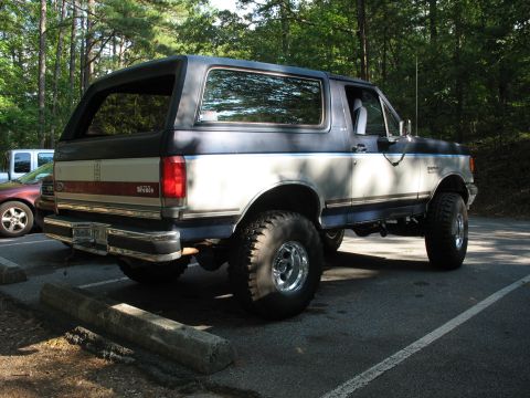 1995 Ford C-350 (Centurion Conversions) - This lifted Ford Bronco is seen from the rear 3/4 angle in a parking lot.