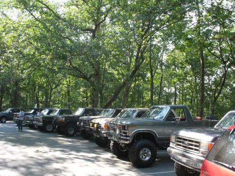 1995 Ford C-350 (Centurion Conversions) - Several lifted pickup trucks, appearing to be from the 1980s, are parked in a line outdoors.
