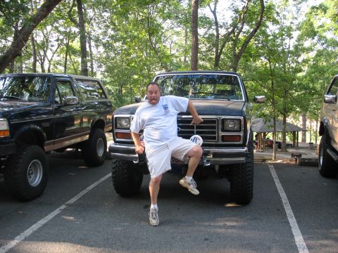 1995 Ford C-350 (Centurion Conversions) - Man playfully poses in front of a lifted Ford truck, with another lifted vehicle to the left.