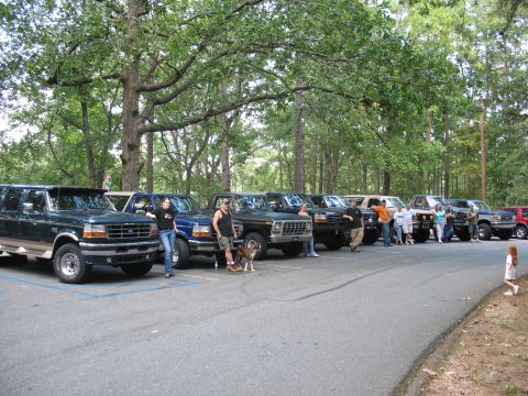 1995 Ford C-350 (Centurion Conversions) - Several Ford trucks and SUVs, including a 1995 Ford C-350 (Centurion Conversions), are parked in a lot under trees.